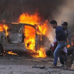 Service burns behind Syrian security agents carrying a man at site of car bombing near the Baath party headquarters and Russian Embassy in central Damascus, Feb 21, 2013, SANA-AP