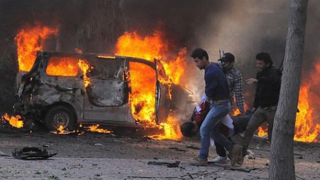 Service burns behind Syrian security agents carrying a man at site of car bombing near the Baath party headquarters and Russian Embassy in central Damascus, Feb 21, 2013, SANA-AP
